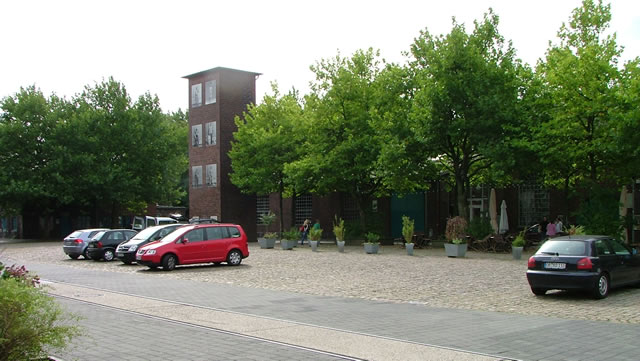 Abb. 7: Der Hofbereich westlich der Walzhallen. Zu erkennen ist der Feuerwehrturm. Hinter den Bäumen befinden sich die ehemalige Schlosserei, Schmiede und Eisenlager